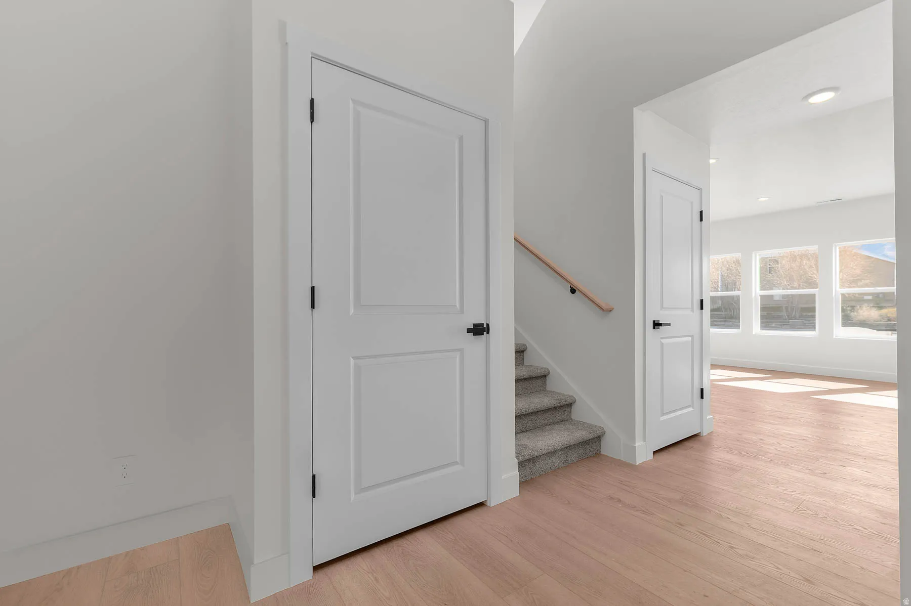 Light wood-finish flooring, white paneled doors with black hardware, carpeted stairs with a wood handrail, and recessed lighting