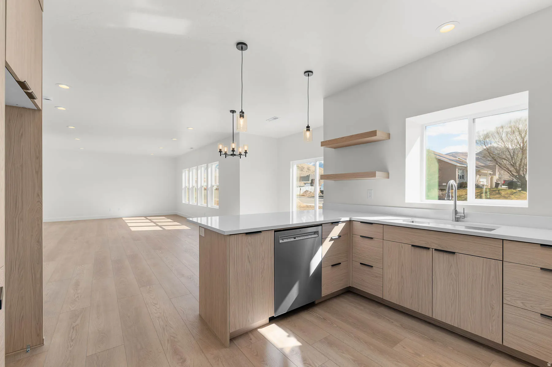 Modern kitchen with light wood-finish cabinetry, white countertops, stainless steel dishwasher, and a large window above the sink