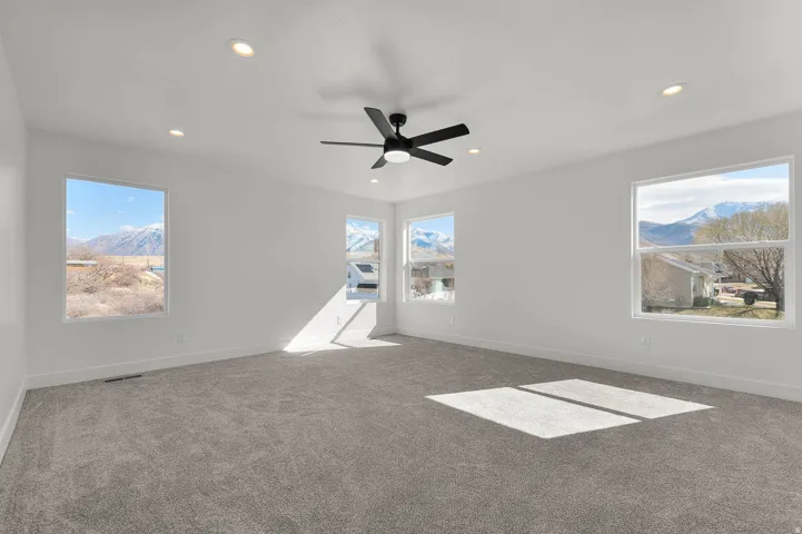 Spacious room featuring neutral carpeting, a contemporary ceiling fan, recessed lighting, and multiple windows with mountain scenery