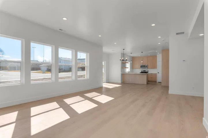 Open-concept living area featuring wood-finish flooring, recessed lighting, multiple windows, and a kitchen with light wood cabinetry and a peninsula