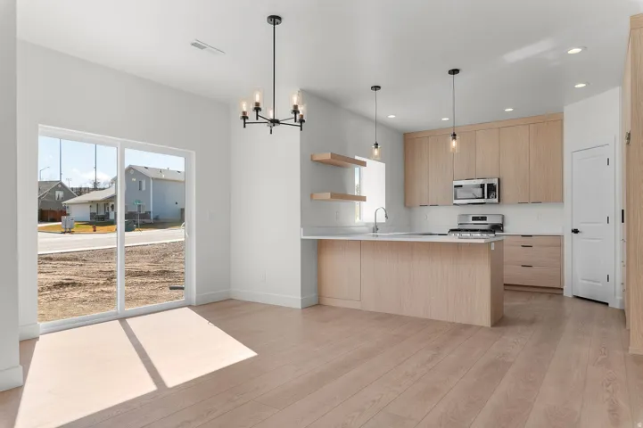 Open-concept kitchen and dining area featuring light wood-finish flooring, a kitchen island with seating, stainless steel appliances, and a sliding glass door