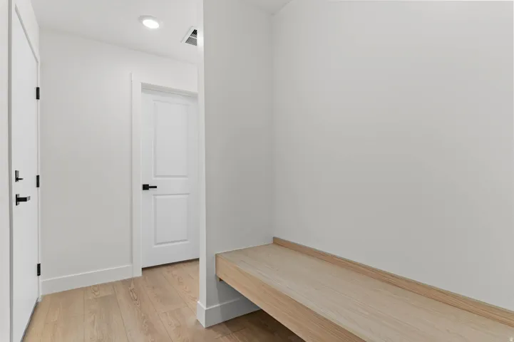 Recessed lighting, light wood-finish flooring, built-in wooden bench, and white paneled doors with black hardware