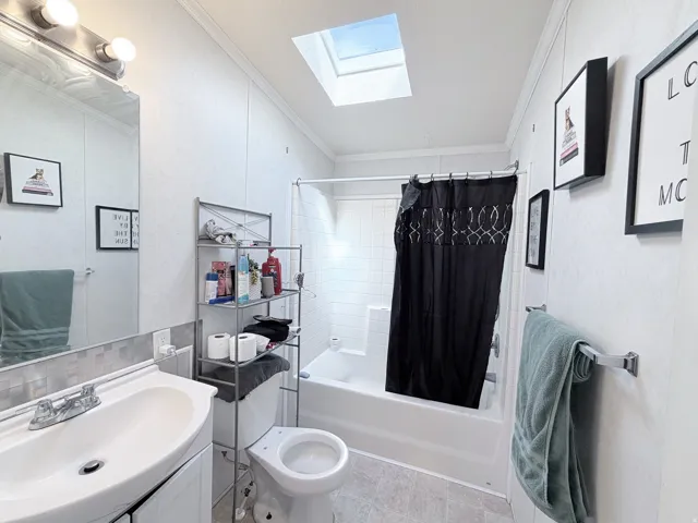 Skylight for natural light, wall-mounted vanity with integrated sink, chrome faucet, tiled backsplash, and full bathtub with shower