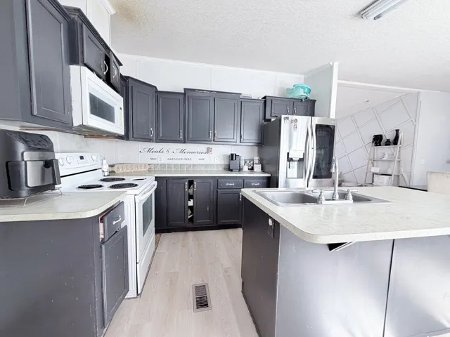 Kitchen featuring dark cabinetry, light countertops, an undermount double-basin sink, and wood-finish flooring