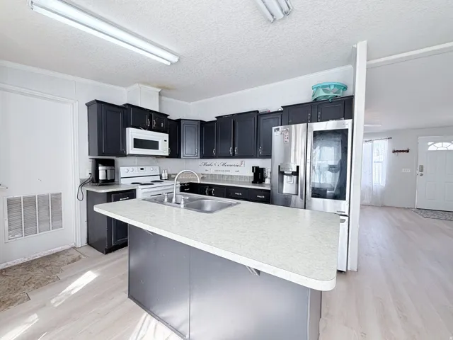 Kitchen featuring dark cabinetry, stainless steel appliances, a center island with a sink, white countertops, and wood-finish flooring