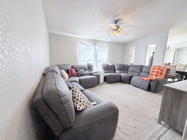 Living area featuring textured walls and ceiling fan with integrated lighting