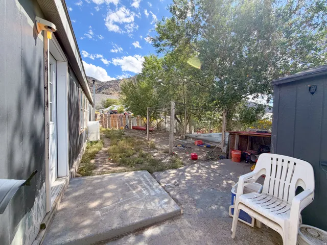 Concrete patio area with a storage shed, mature trees, and a partial fence