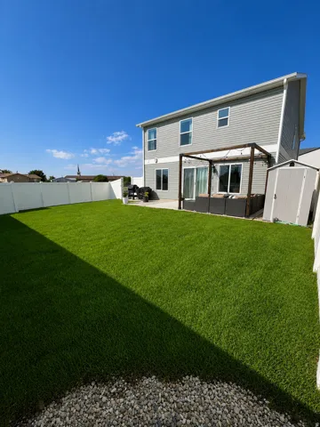Expansive rear yard featuring green lawn, a white privacy fence, and a gravel border
