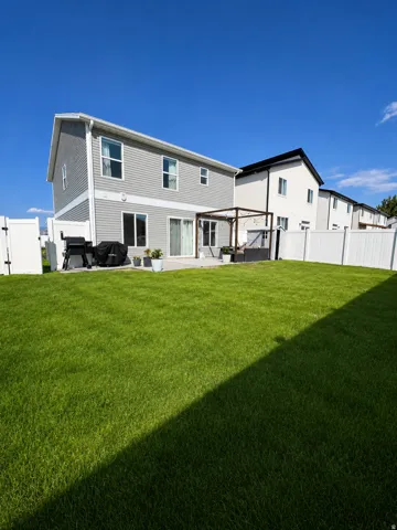Expansive backyard with a manicured lawn, full privacy fencing, and a built-in pergola over a patio area