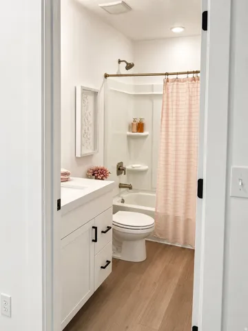 White vanity with black pulls, white countertop, wood-finish flooring, and a white tub with integrated shower