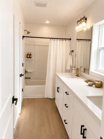 Double vanity with white cabinetry and integrated sinks, wood-finish flooring, a full-size bathtub with shower, recessed lighting, and a window providing natural light