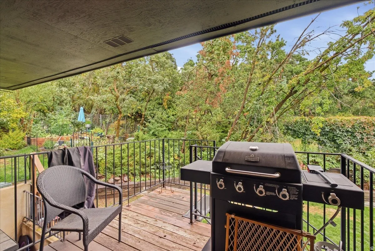 Covered patio with wood-finish flooring, black metal railing, and lush perimeter landscaping