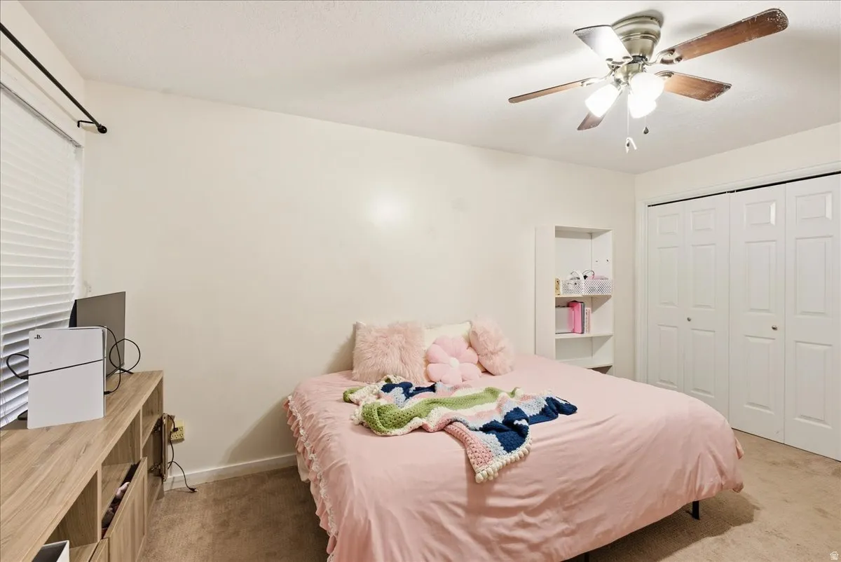 Ceiling fan with light fixture, built-in shelving, bifold closet doors, and carpeted flooring