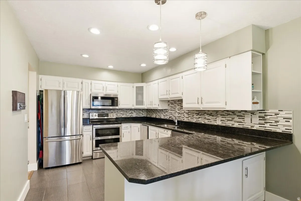 Kitchen featuring white cabinetry, dark stone countertops, stainless steel appliances, and a mosaic tile backsplash