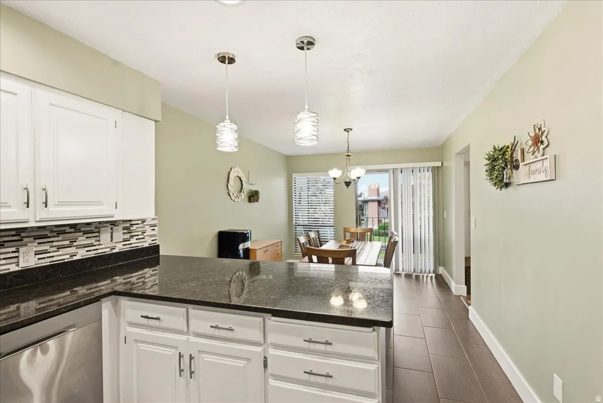 Kitchen featuring white cabinetry, dark stone countertops, a mosaic tile backsplash, and stainless steel appliances