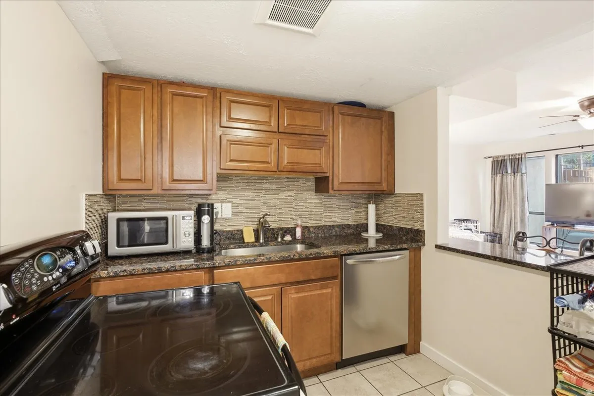 Kitchen featuring wood cabinetry, a mosaic tile backsplash, a stainless steel dishwasher, and a granite-style countertop