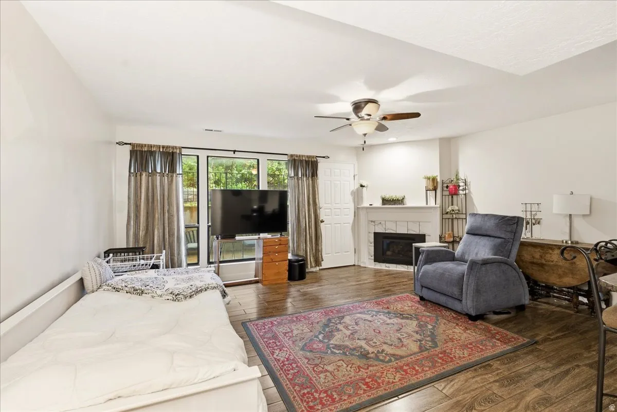 Wood-finish flooring, white walls, ceiling fan, glass-paneled door, and a fireplace with a white mantel
