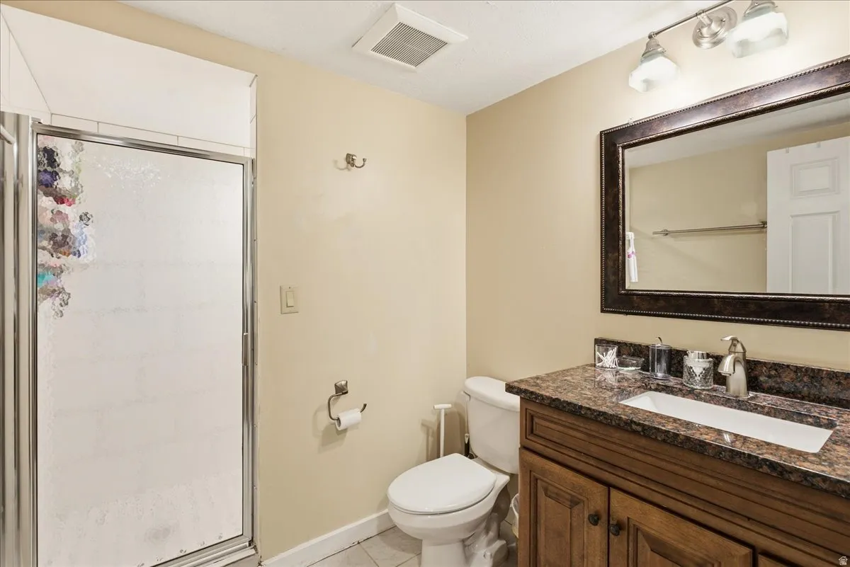 Shower with frosted glass enclosure, single vanity with brown cabinetry, countertop with integrated white sink, framed mirror, and wall-mounted light fixture