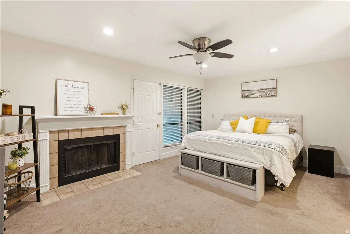 Carpeted flooring, recessed lighting, ceiling fan, tile-surround fireplace with mantel, and a paneled door