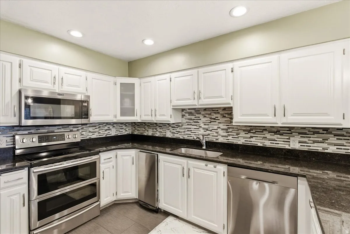 White cabinetry with stainless steel appliances, dark countertops, and a tiled backsplash