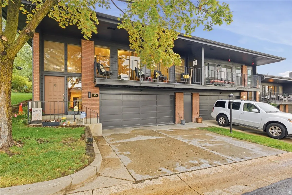 Modern-style exterior featuring a prominent brick facade, multiple balconies with metal railings, a dual-door garage, and large expansive windows