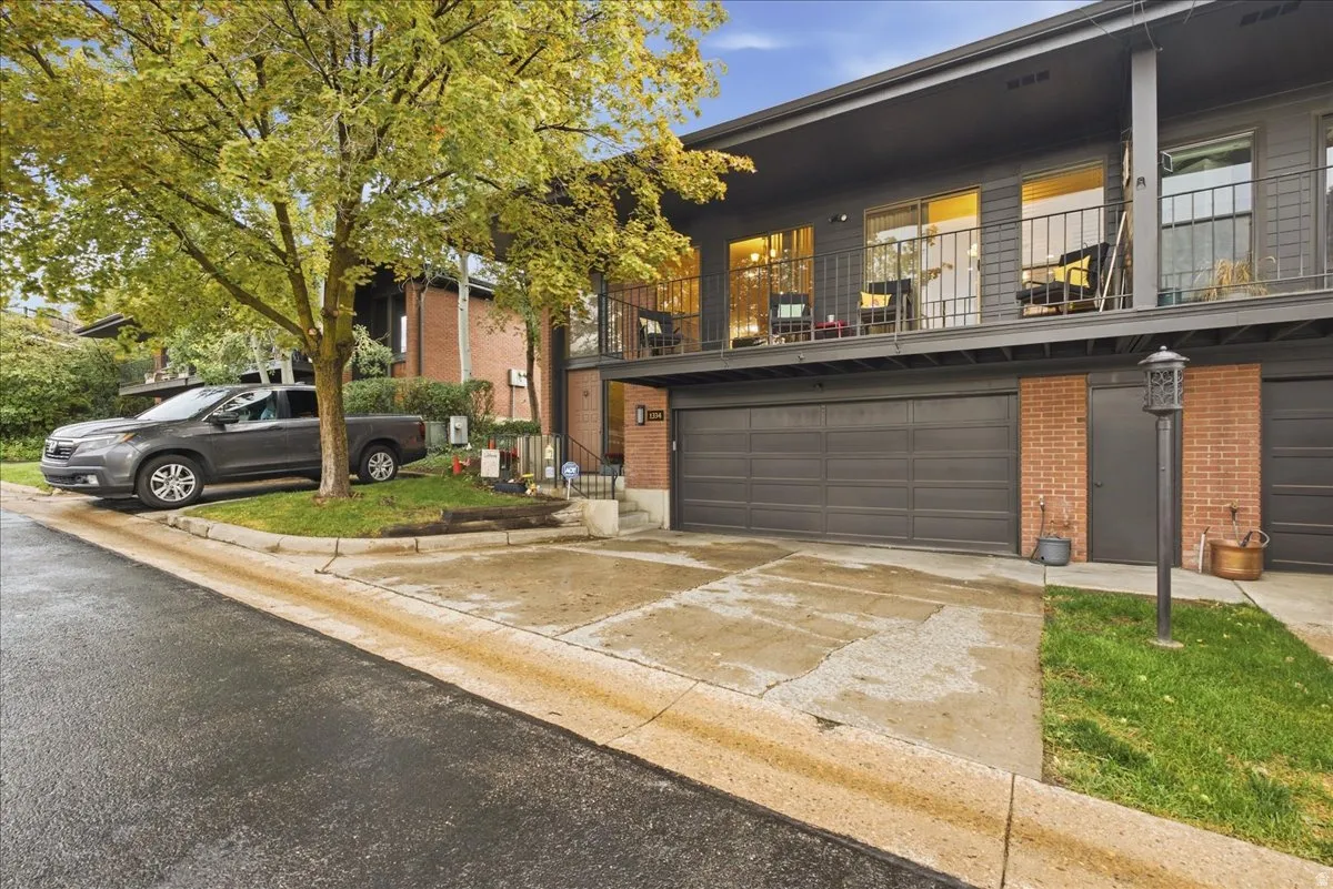 Attached double garage with dark gray doors, a private balcony with metal railings, and a brick-clad entry