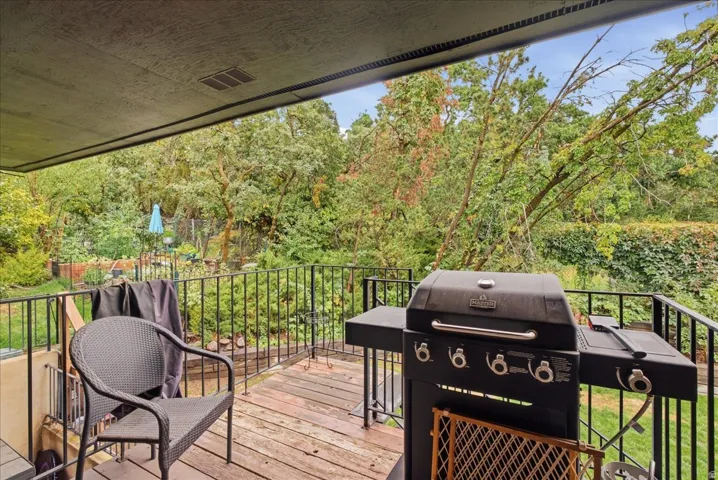 Covered patio with wood-finish flooring, black metal railing, and lush perimeter landscaping