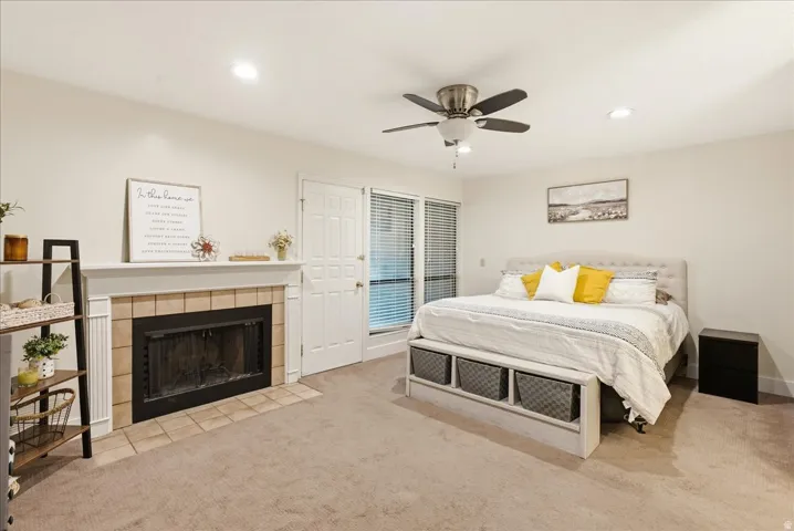 Carpeted flooring, recessed lighting, ceiling fan, tile-surround fireplace with mantel, and a paneled door