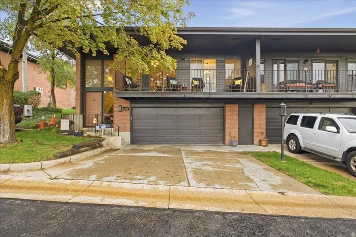 Contemporary exterior with a brick and gray facade, featuring a private balcony with metal railings, an integrated garage, and a concrete driveway