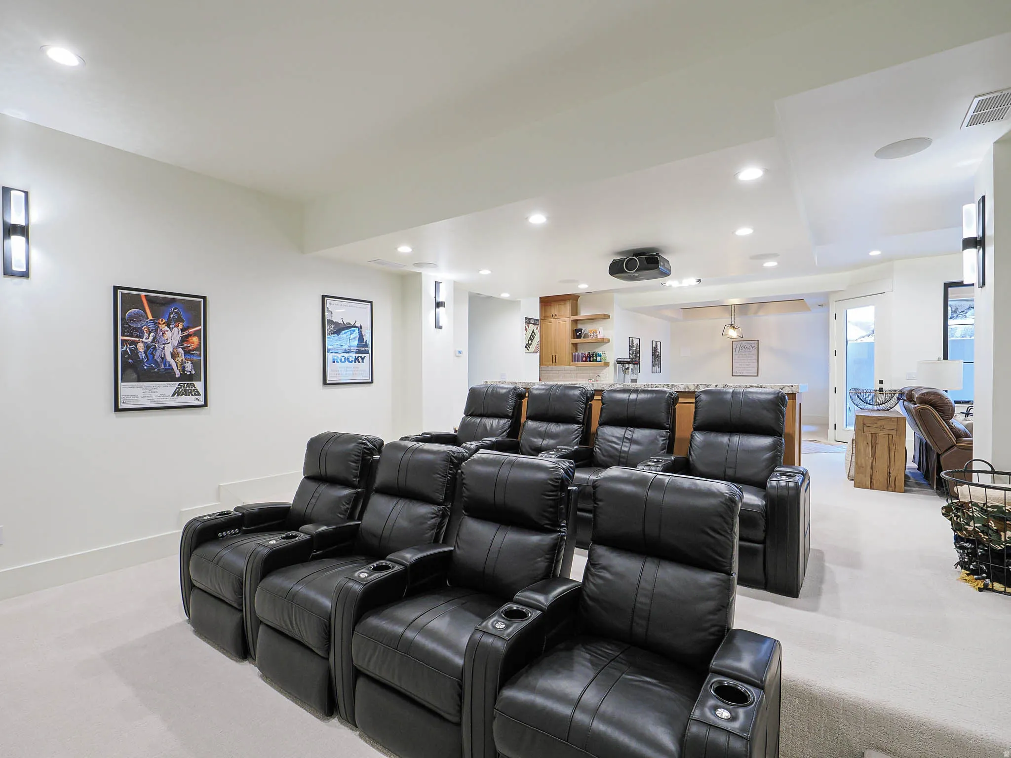 Theater room featuring tiered seating, recessed ceiling lighting, a ceiling-mounted projector, and a built-in wet bar with wood cabinetry and shelving