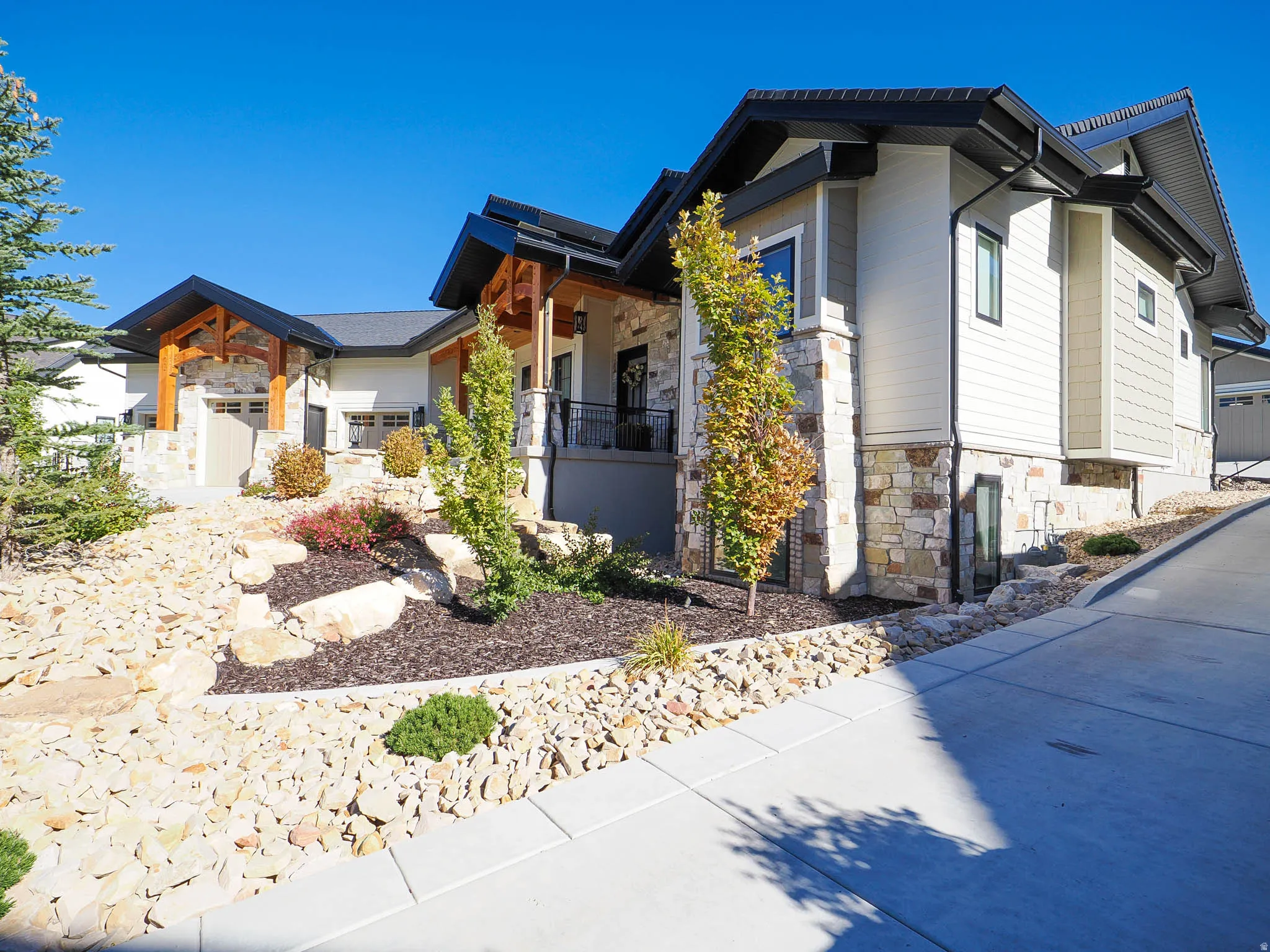 Contemporary home with stone and siding exterior, a dark shingle roof, and a concrete driveway