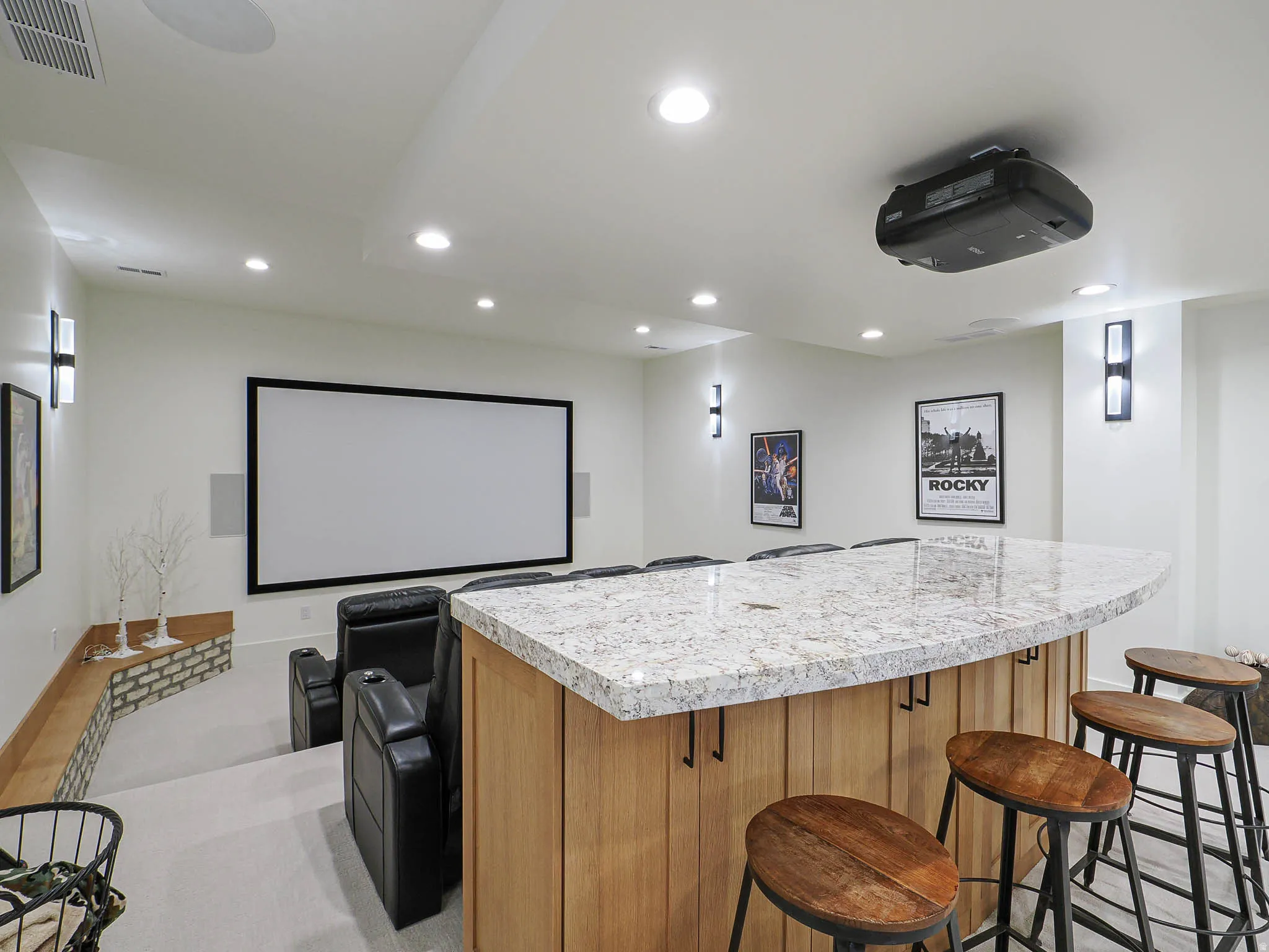 Curved stone-finish countertop bar with wood-finish paneling, recessed lighting, wall sconces, large projection screen, and a ceiling-mounted projector