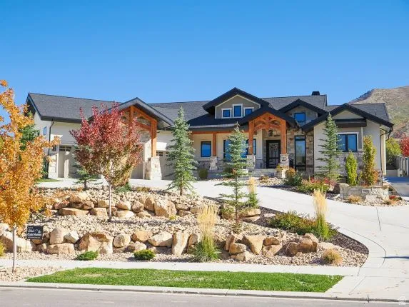 Two-car garage with stone accents, wood-beam entry, landscaped front yard with decorative boulders, and concrete driveway
