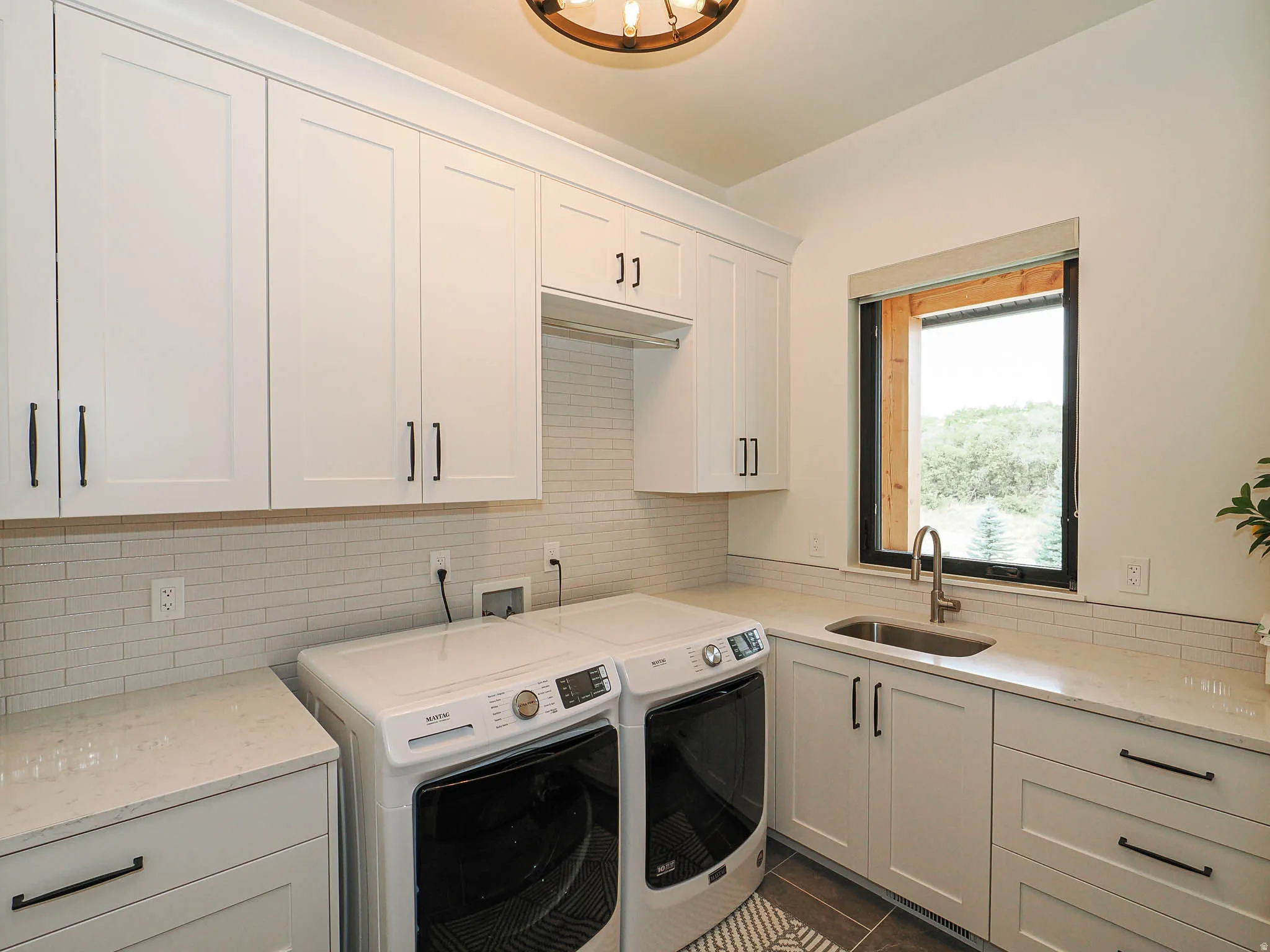 White shaker-style cabinetry with matte black hardware, light quartz countertops, a subway tile backsplash, a stainless steel sink with a gooseneck faucet, and a large window with black trim