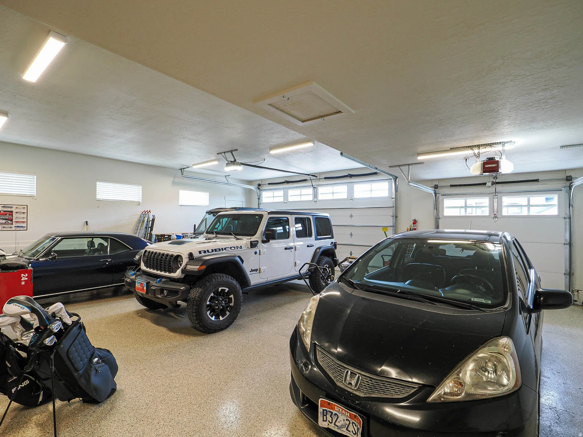 Attached three-car garage featuring two overhead doors with window accents, an epoxy-coated concrete floor, and multiple overhead fluorescent light fixtures