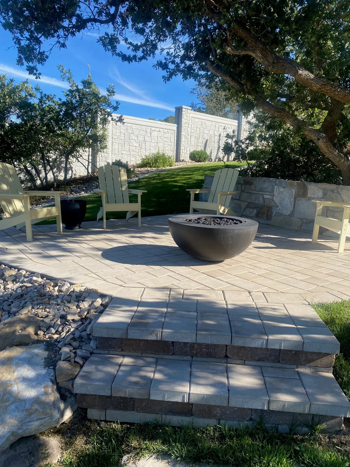 Paver patio featuring a built-in fire pit, stone retaining wall, and block privacy fence