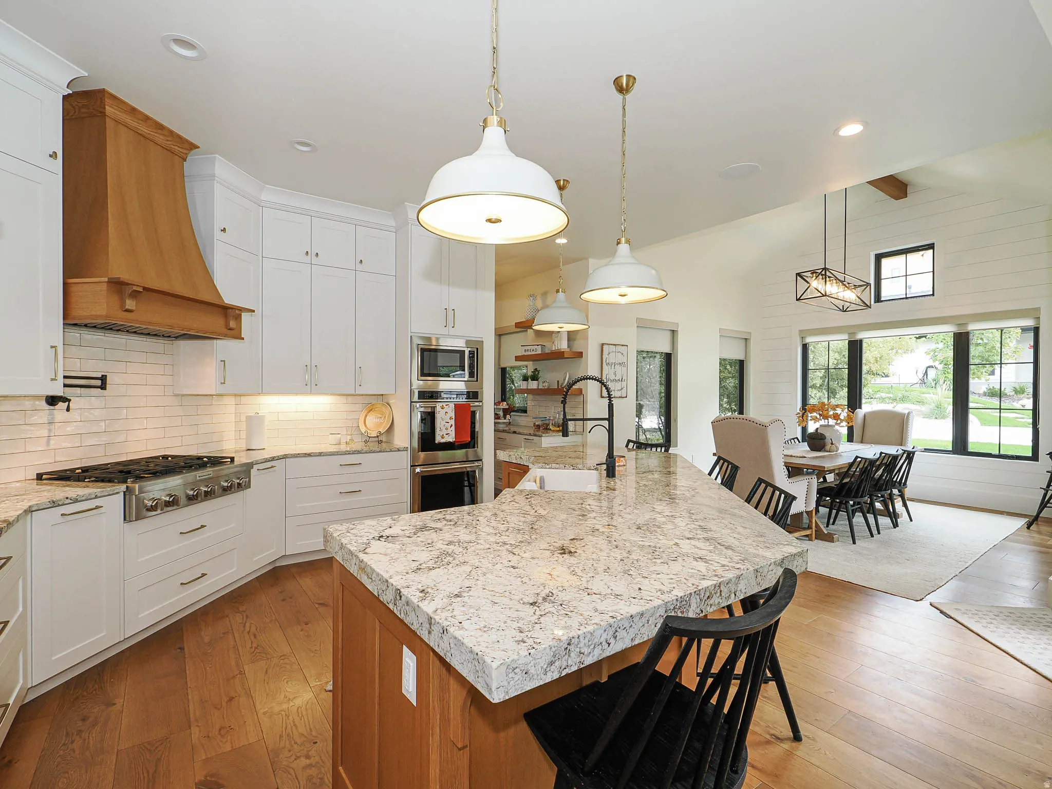 Gourmet kitchen with wood-finish flooring, white cabinetry, a wood range hood, and a spacious island with a stone countertop