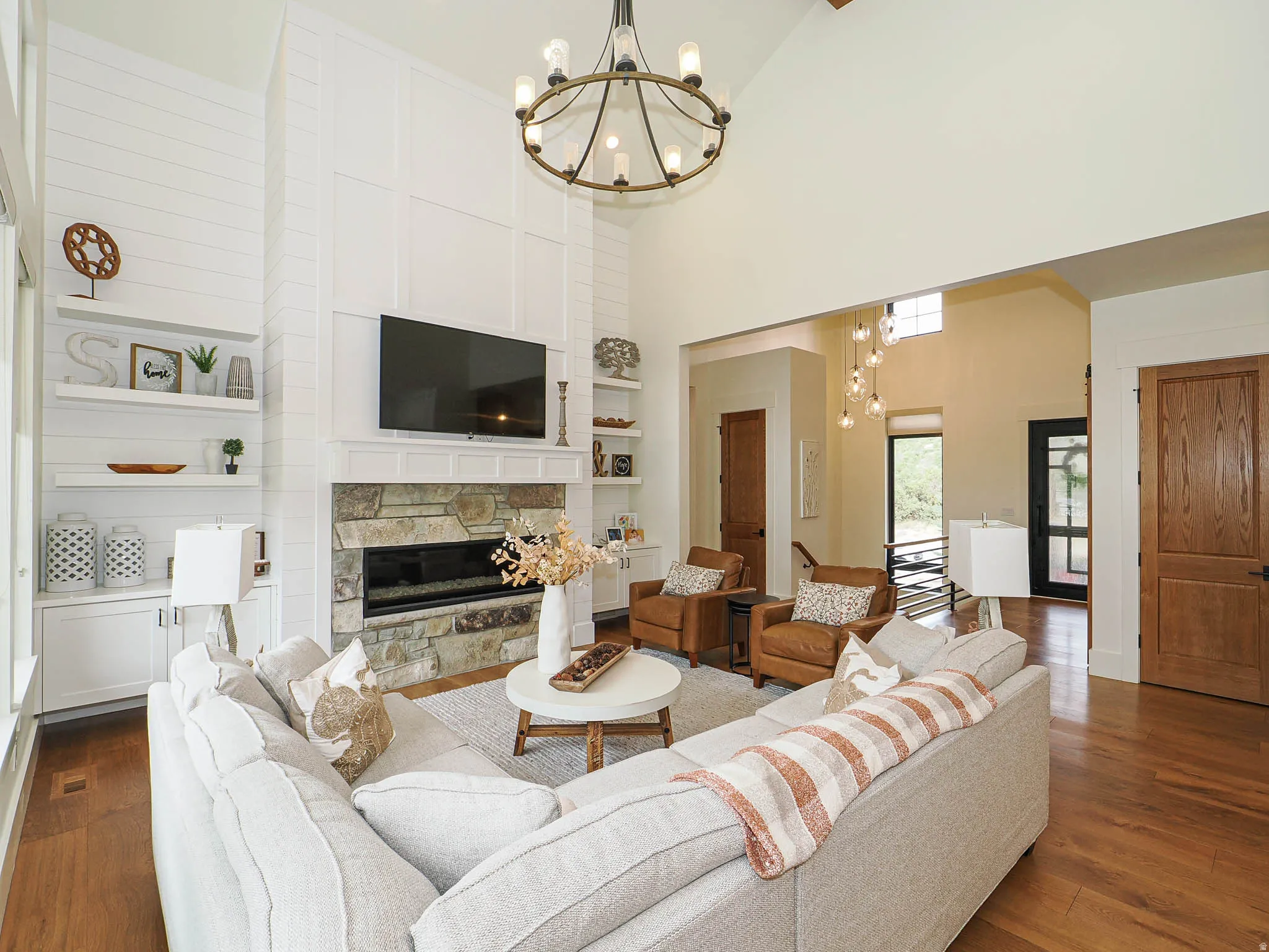 Vaulted ceiling with an exposed beam, stone fireplace with a linear insert, built-in shelving, wood-finish flooring, and a decorative chandelier