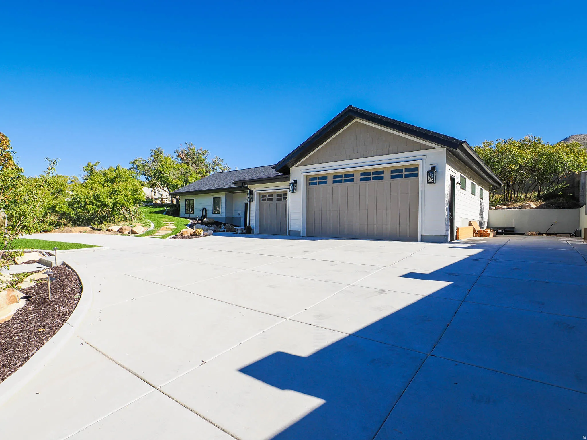 Expansive concrete driveway, attached two-car garage with carriage-style doors, additional single-car garage, and exterior wall lanterns