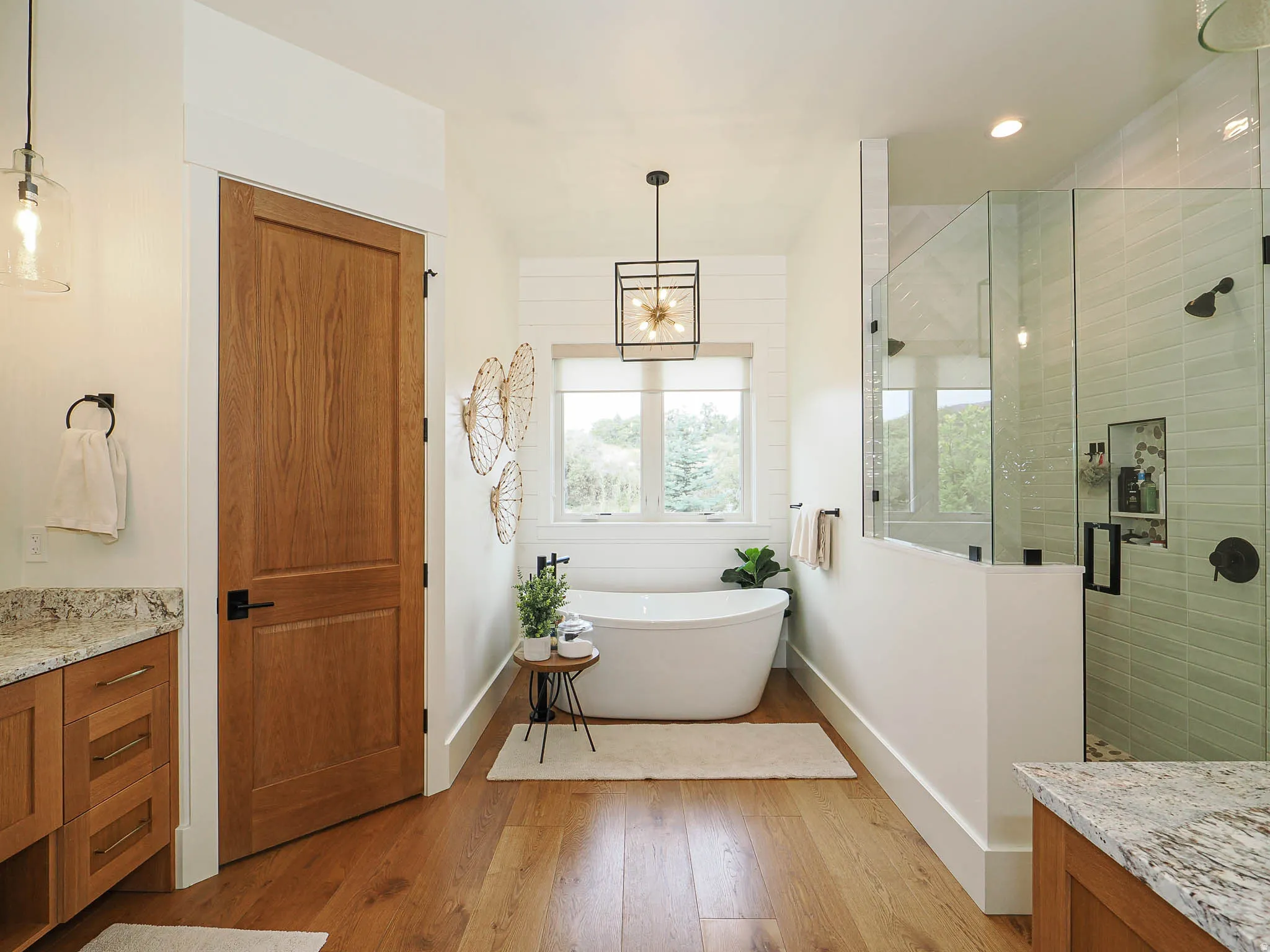 Freestanding soaking tub, walk-in shower with glass enclosure, wood-finish flooring, wood cabinetry with stone countertop, and custom light fixtures