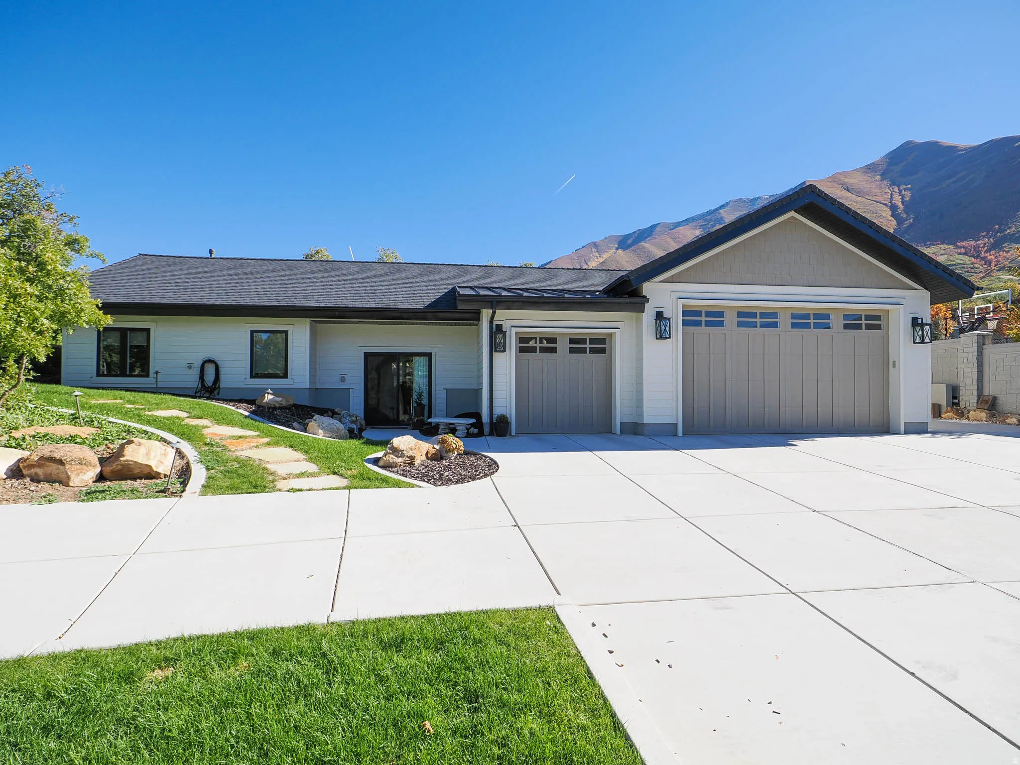 Contemporary exterior with white siding and dark trim, featuring a multi-car garage with panel doors, a paved driveway, and a landscaped front yard with a stone pathway