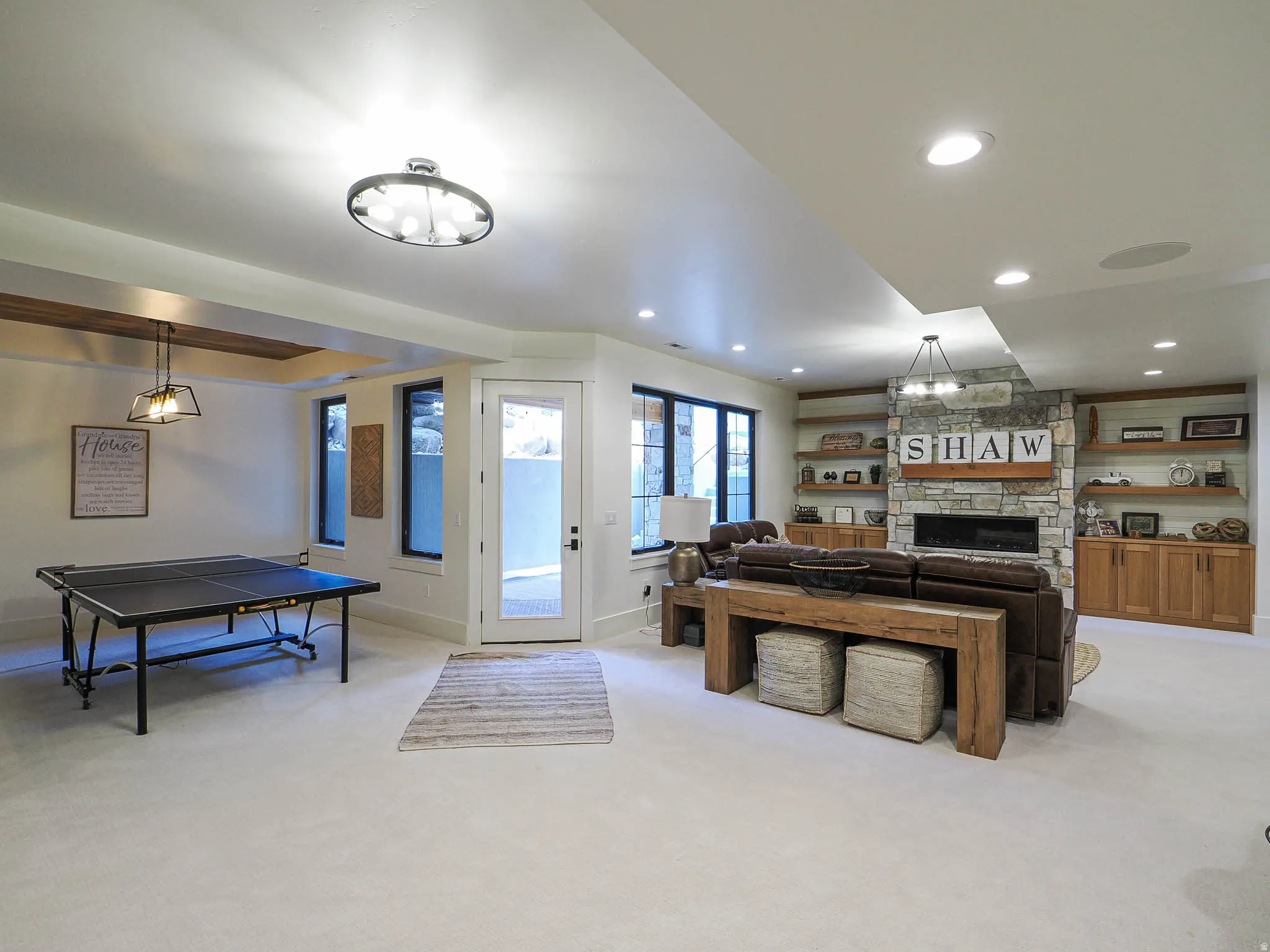 Recessed lighting, stone-clad fireplace, integrated shelving, built-in cabinetry, and a glass-paneled door