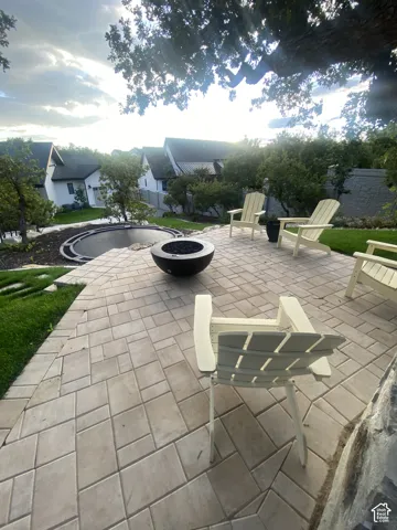 Paved patio with a fire pit, surrounded by manicured landscaping and mature trees