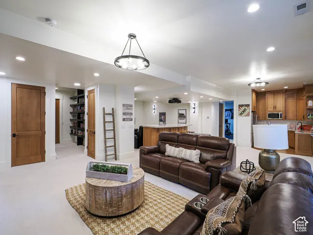 Recessed lighting and a decorative chandelier illuminate a spacious room featuring a built-in entertainment bar, warm wood cabinetry, and a dedicated shelving alcove