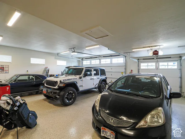 Attached three-car garage featuring two overhead doors with window accents, an epoxy-coated concrete floor, and multiple overhead fluorescent light fixtures