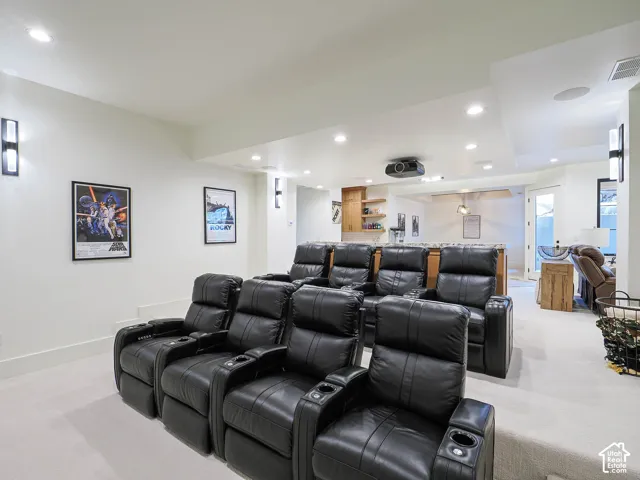 Theater room featuring tiered seating, recessed ceiling lighting, a ceiling-mounted projector, and a built-in wet bar with wood cabinetry and shelving
