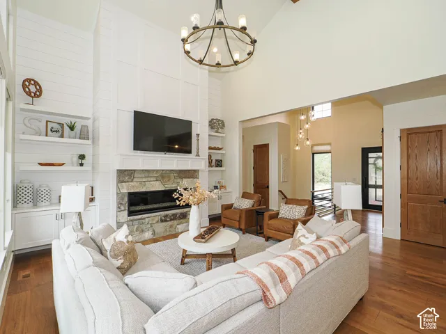 Vaulted ceiling with an exposed beam, stone fireplace with a linear insert, built-in shelving, wood-finish flooring, and a decorative chandelier