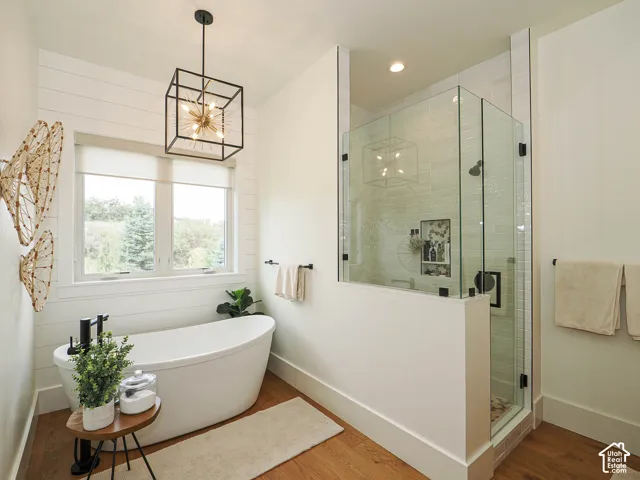 Freestanding soaking tub with matte black fixtures, glass-enclosed shower with tile surround, wood-finish flooring, and white shiplap wall accent