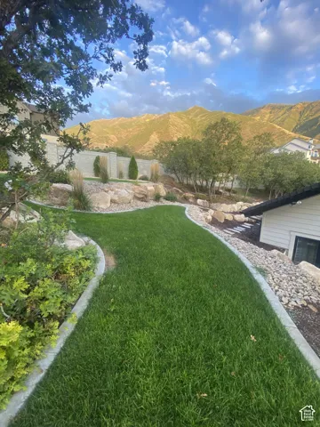 Manicured lawn with concrete edging, featuring a stone retaining wall and mature landscaping