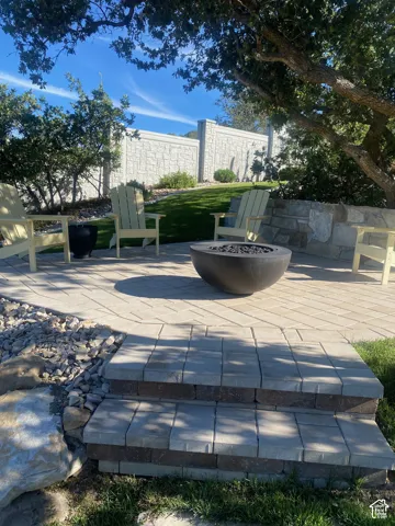 Paver patio featuring a stone fire pit, tiered landscaping, stone retaining wall, and a decorative privacy wall